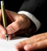 Closeup of male hand signing legal or insurance document on black desk with reflection.