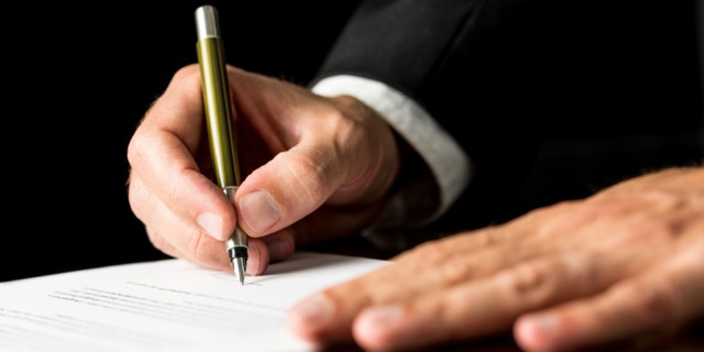 Closeup of male hand signing legal or insurance document on black desk with reflection.